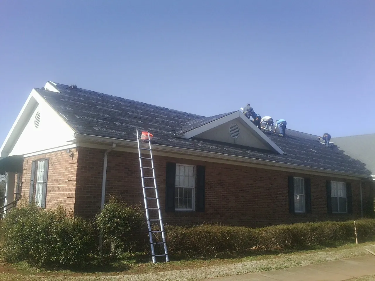 Crew tearing shingles off a brick ranch roof with a ladder set — Metal Roof Repair work by our crew in East Hartland