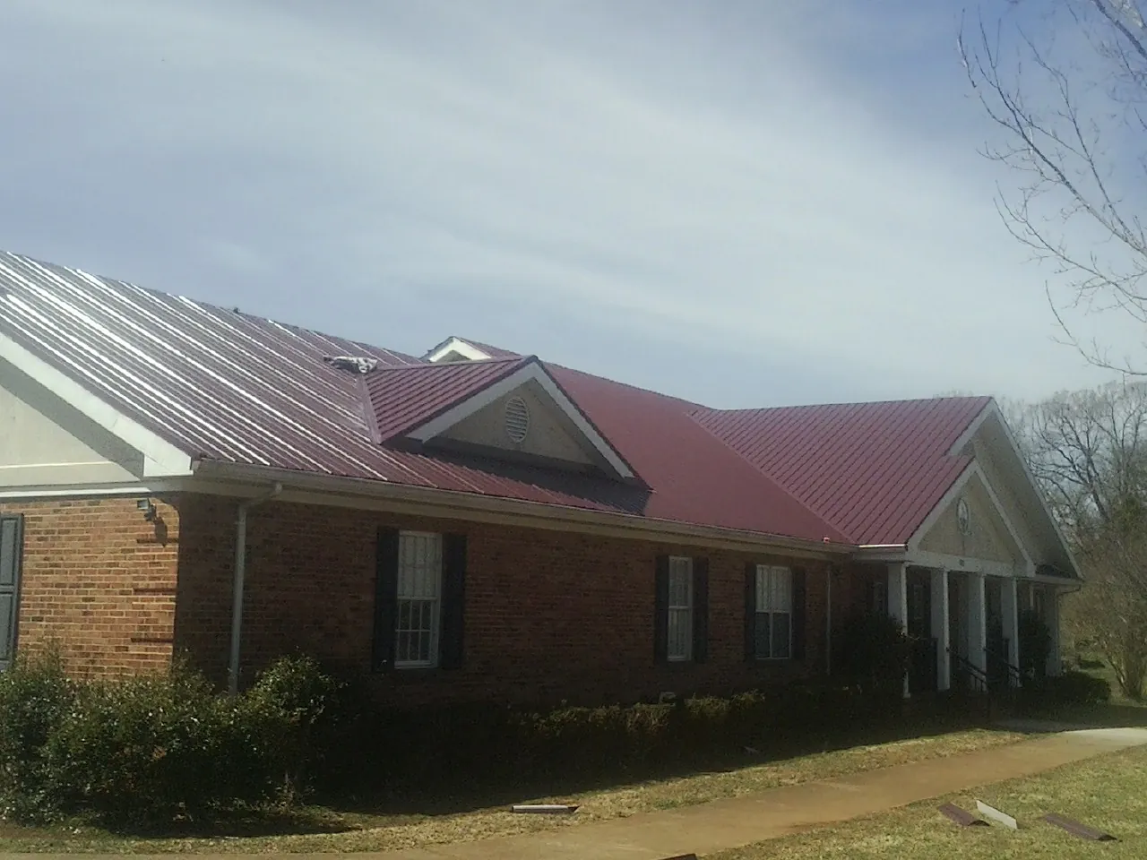 Red metal roof with gabled entries on a long brick building, from a Hail Damage Roof Repair job in East Hartland