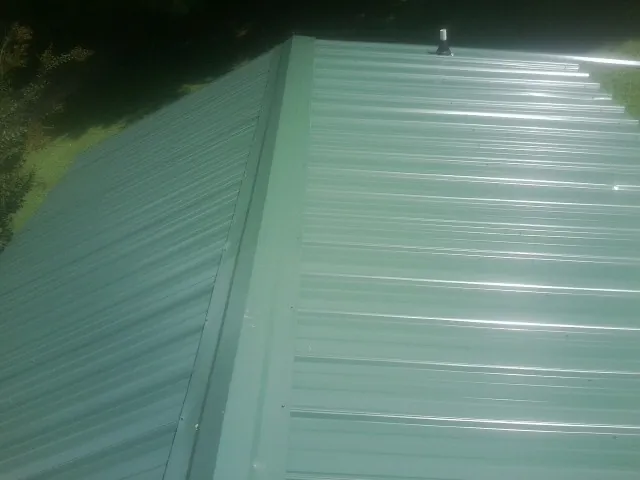 New green metal panels meeting at the ridge of a roof — Flat Roof Repair work by our crew in East Hartland