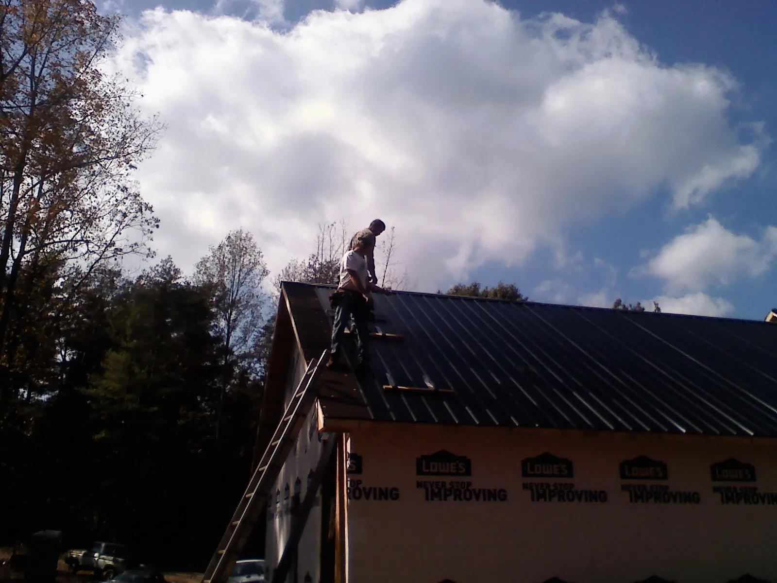 Roofer fastening dark metal panels high against a cloudy sky, from a Roof Inspection job in East Hartland