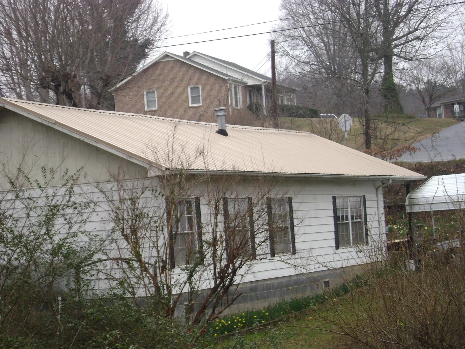 Tan metal roof on a white sided house set into a hillside — Commercial Roofing by Roofing Brothers in East Hartland